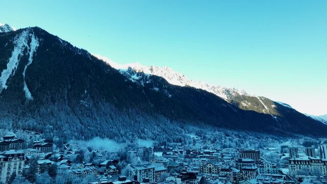 Slow drone rise up of Chamonix ski town in the french alps winter morning with snow on ground.