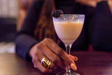 An elegant hand cradles a sophisticated cocktail, garnished with a plump blackberry. The creamy...