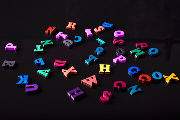 Scattered colored letters on a black background. Reading or education concept.