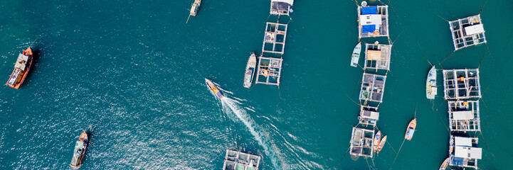Aerial view of boats and floating fish pens on a calm blue sea, depicting aquaculture or maritime...