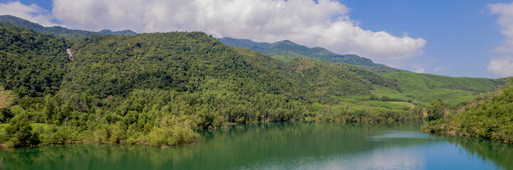 Panoramic view of a tranquil lake with lush green forested mountains under a clear blue sky, suitable for environmental or travel-related concepts