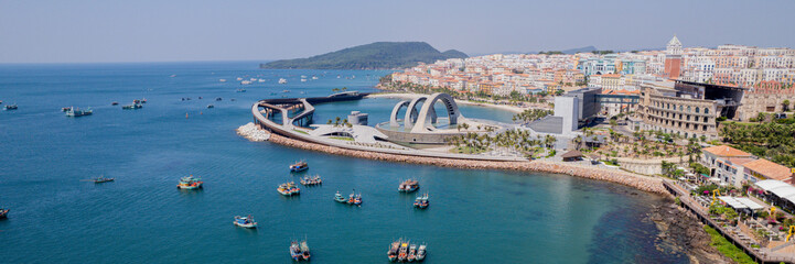 Aerial panoramic view of a coastal city with modern architecture juxtaposed against traditional waterside buildings, highlighting urban development and cultural blend