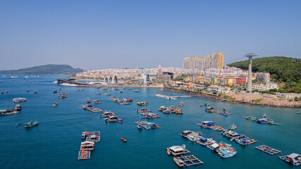 Aerial view of a coastal cityscape with boats anchored in blue waters and a cable car system...