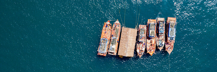 Aerial view of a cluster of fishing boats on a tranquil blue ocean, depicting a maritime or seafood concept - obrazy, fototapety, plakaty