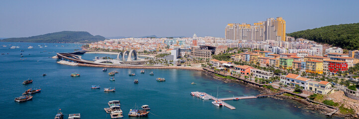 Panoramic aerial view of a vibrant coastal city with colorful buildings, modern architecture, and boats dotting the harbor on a clear day