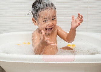 happy infant baby take a bath and playing under a shower in bathtub