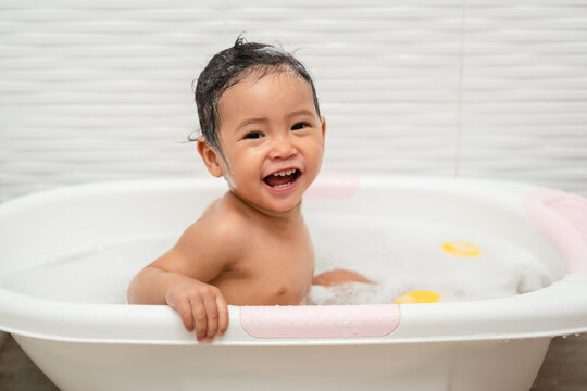 happy infant baby take a bath and playing with foam bubbles in bathtub