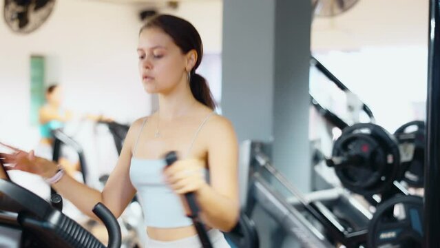 Slender athletic girl during cardio exercises on elliptical simulator in fitness center. Sports to max. Electronic tracking for most productive workout