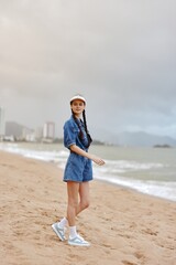Alone, Sad and Standing: A Pretty Young Woman in a Blue Dress on the Beach, Looking at the Ocean with a Sad Expression, Embracing the Relaxation of a Tropical Paradise