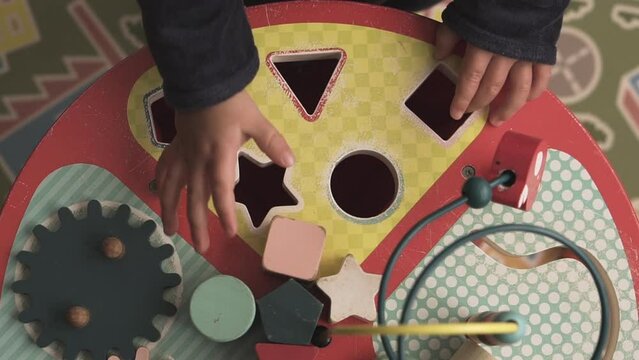 Top view of a baby failing to fit shapes and pieces into a table. Children playing and learning with educational wooden toys