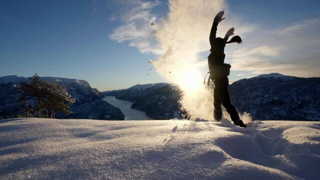 Young woman throws snow up in the air in front of sunset, Hiking Norway fjords