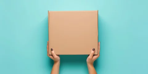 Foto op Aluminium Top view to female hand holding brown cardboard box on light blue background. Mockup parcel box. Packaging, shopping, delivery concept © StockWorld