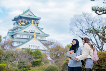 Fototapeta na wymiar Travel, muslim travel, woman girl tourist Two Asian friends but different religions walking at Osaka Castle, Osaka Castle is one of the most famous landmarks in Japan and Osaka, holiday lifestyle.