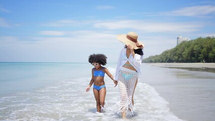 Happy African family enjoy and fun outdoor lifestyle travel at the sea on summer beach holiday vacation. Mother and little daughter holding hands together and walking on tropical beach in sunny day.
