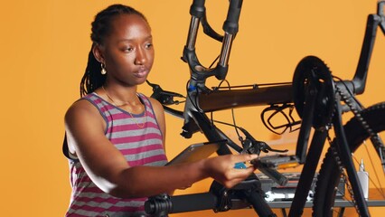 African american woman following online tutorials on tablet, learning to repair her damaged bike. Cycling hobbyist following instructions on how to do upkeeping for bicycle parts, studio background
