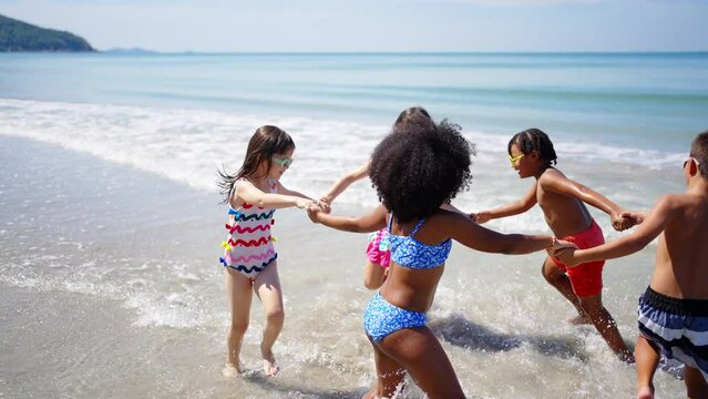 Group of Children kid enjoy and fun outdoor lifestyle travel ocean on summer beach holiday vacation. Diversity child boy and girl friends running on the beach and playing sea water at tropical island.