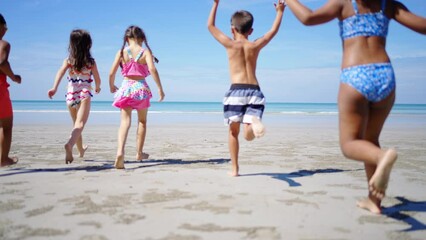 Happy children travel and playing at the beach on summer holiday vacation. Group of Little child boy and girl kids enjoy and fun outdoor lifestyle running and playing in the sea at tropical island.