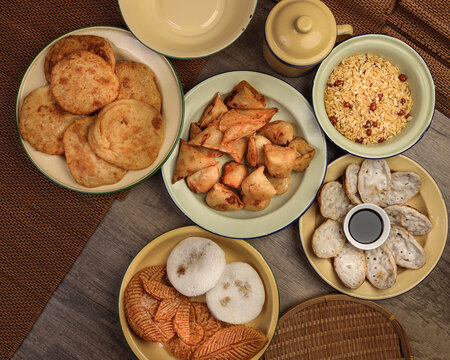 Bengali sweet savoury snacks variety stuffed pancake chitoi bhapa nakshi pakkon pitha singara samosa dal aloo puri fried flattened rice cheera mix on enamel tin metal plate over rustic background