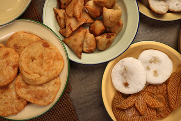 Bengali sweet savoury snacks variety stuffed pancake chitoi bhapa nakshi pakkon pitha singara samosa dal aloo puri fried flattened rice cheera mix on enamel tin metal plate over rustic background