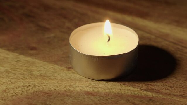 Closeup: One tea candle on wooden countertop is lit with burning match