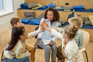 High angle view at group of excited children high five with female therapist after support group...