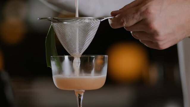 Dolly shot of a bartender straining a paloma through a mesh strainer into a glass