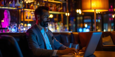 Obraz premium Businessman working late at a laptop in a vibrant bar. elegant setting with neon lights. modern remote work lifestyle image. AI