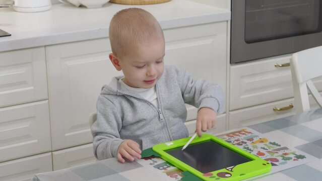 3-year-old child drawing with pen on electronic drawing writing board. Little boy playing with drawing tablet for kids.