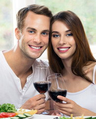 Portrait image of smiling amorous couple drinking red wine. Caucasian models with redwine glasses in love concept. Happy man and woman posing together home house indoors.