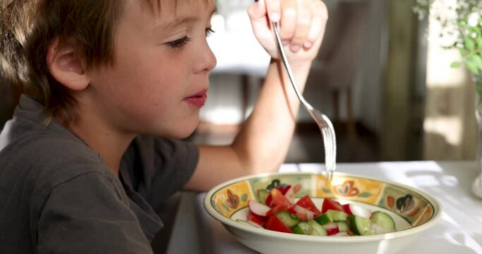 Hungry boy eats vegetable salad sitting at table in grandmother country house. Calm atmosphere in apartment in sunny weather. Satisfying hunger