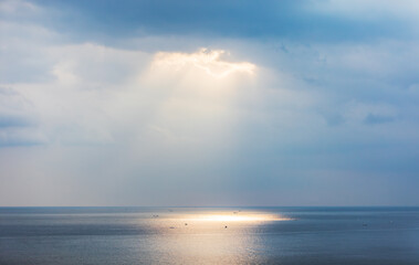 Fototapeta na wymiar Sunlight pouring through the clouds reflects on the surface of the sea. Morning sunrise scenery on the sea