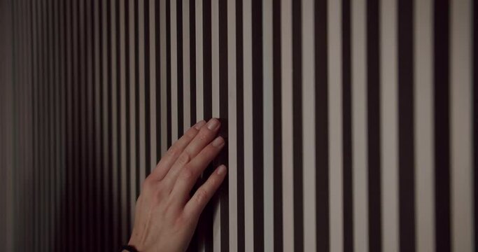 Closeup of female hand touching wall decorated wooden panels at apartment with modern interior. Cropped view on woman checking wood plank wall after renovation. Natural materials