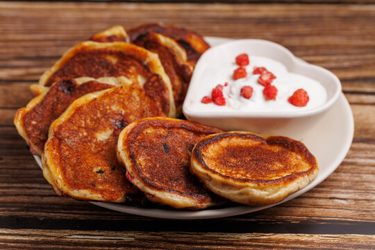 Pancakes with sour cream on the wooden table. Russian fritters oladyi with berries. Close up, rustic, heart shape bowl
