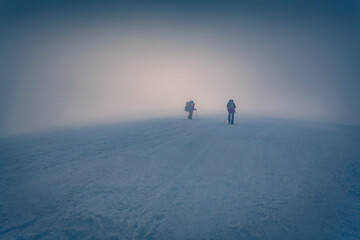 Two tourists climbing to the top of summit. Foggy winter scene of Carpathian mountains, Ukraine,...