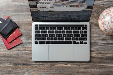 A laptop, passport, credit card are on the table. Conceptual image of booking and planning a sea cruise.