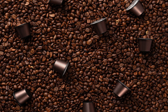 Top view of many roasted coffee beans and brown capsules for coffee machines.