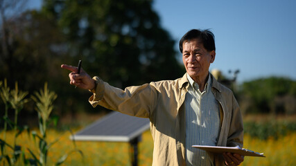 Mature farmer standing front of solar panels in a smart agricultural farm. Renewable energy and...