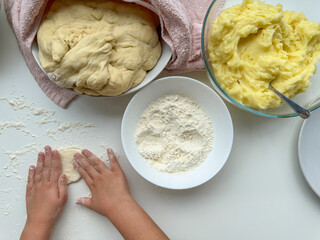The hands of child knead the dough for making pies on white table, top view.