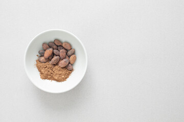 Closeup top down view of a plate with cocoa beans and cacao powder on a light neutral background with copy space