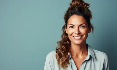 Fotobehang Confident Mature Businesswoman with Bun Hairstyle Smiling in Light Blue Blouse Against a Soft Blue Background © Bartek