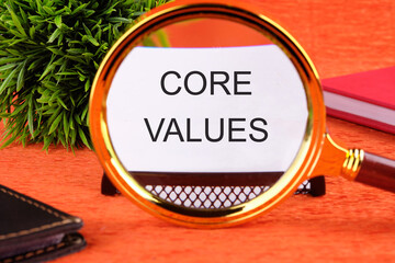 CORE VALUES word written on a business card through a magnifying glass on an orange background