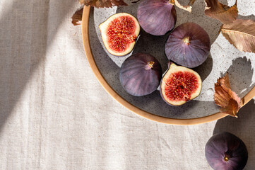 Fresh fig fruits on plate on beige linen tablecloth background with dried leaves an natural sunlight shadows, aesthetic lifestyle healthy vitamin food