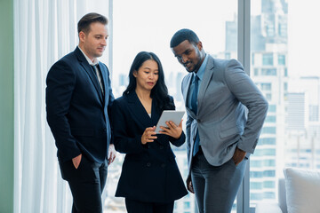 Diverse smart businesspeople standing near window with skyscraper while looking at business data...