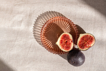Whole and cut figs on neutral beige table and on plate with aesthetic sun light shadows, minimal...