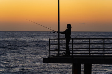 Fototapeta premium Fishing on the Brighton Jetty at sunset. Adelaide, South Australia.