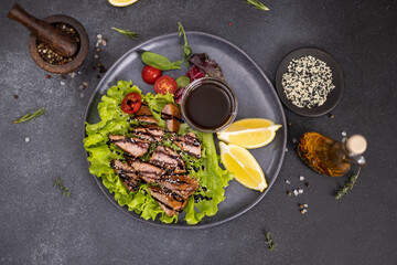 pieces of Organic grilled Tuna Steak on black ceramic serving dish with salad on a table