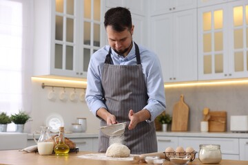 Fototapeta na wymiar Making bread. Man sprinkling flour onto dough at wooden table in kitchen