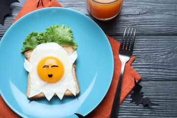 Halloween themed breakfast served on black wooden table, flat lay. Tasty toast with fried egg in...