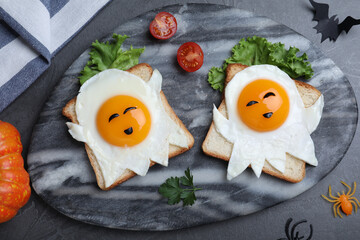 Halloween themed breakfast served on black table, flat lay. Tasty toasts with fried eggs in shape...