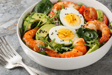 Balanced breakfast salad with shrimp, avocado, arugula, spinach, tomatoes and boiled eggs close-up on a bowl on the table. Horizontal
